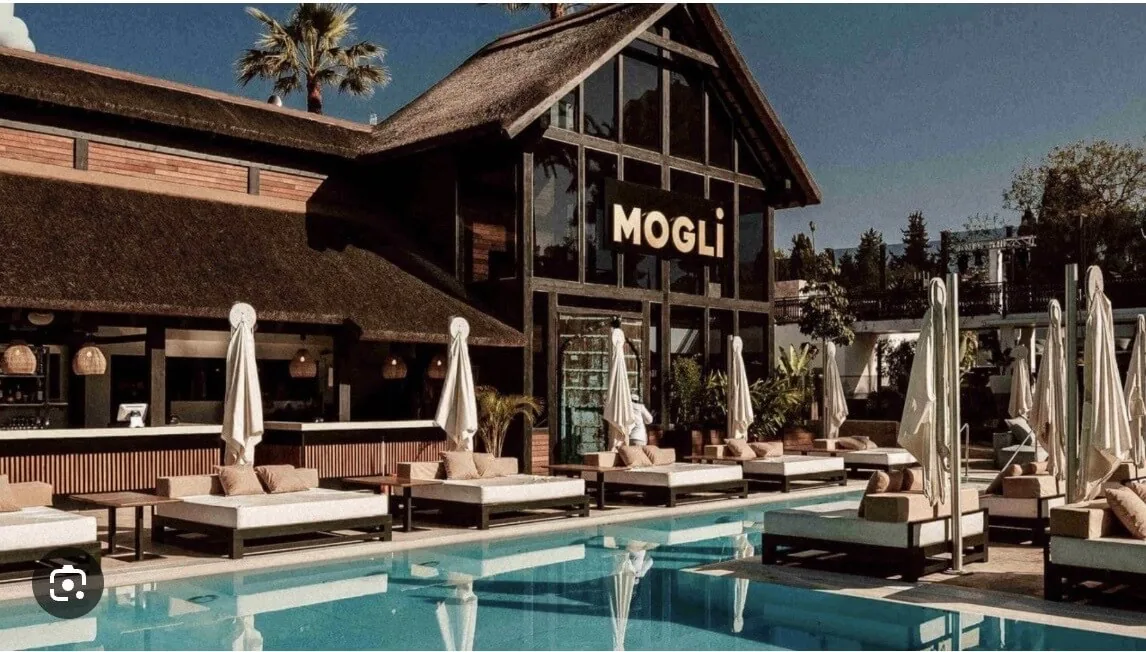 Exclusivo club de playa y piscina Mogli Marbella con arquitectura de techo de paja y lujosas tumbonas alrededor de la piscina