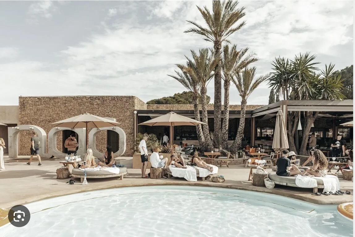 Nao Pool Club Marbella, piscina de lujo bohemio con palmeras, camas de día y las letras NAO de piedra distintivas en Cabopino