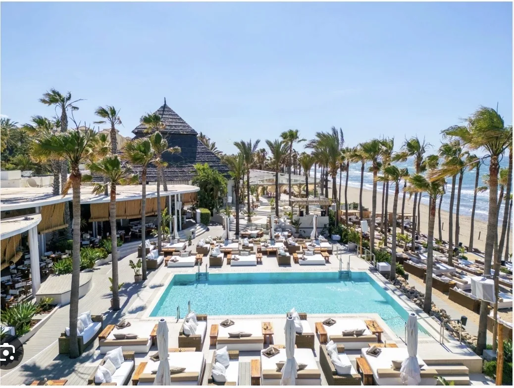 Club de playa de lujo Nikki Beach Marbella con las características tipis blancas, palmeras y elegantes tumbonas frente a la playa