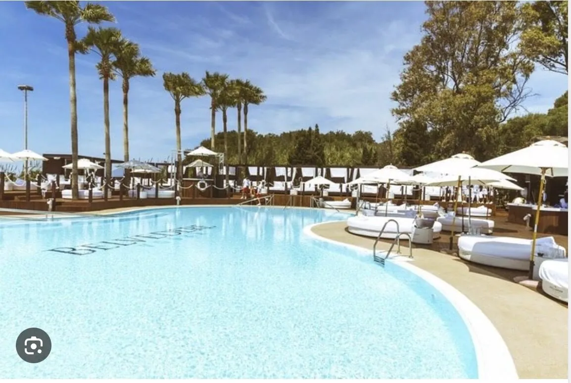 Club de piscina de lujo Opium Beach Marbella con camas balinesas VIP blancas, palmeras y piscina de agua salada turquesa